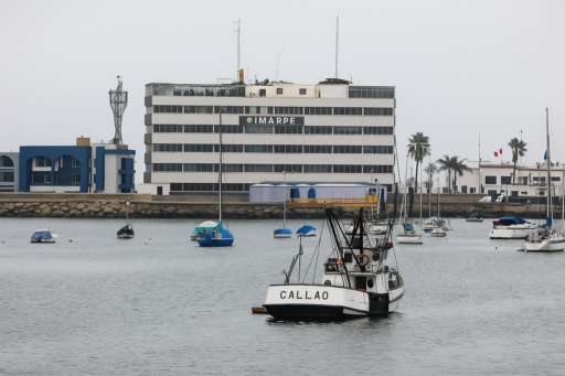 Vista del edificio de IMARPE en el Callao frente al mar, con varias embarcaciones pesqueras y veleros anclados en la bahía